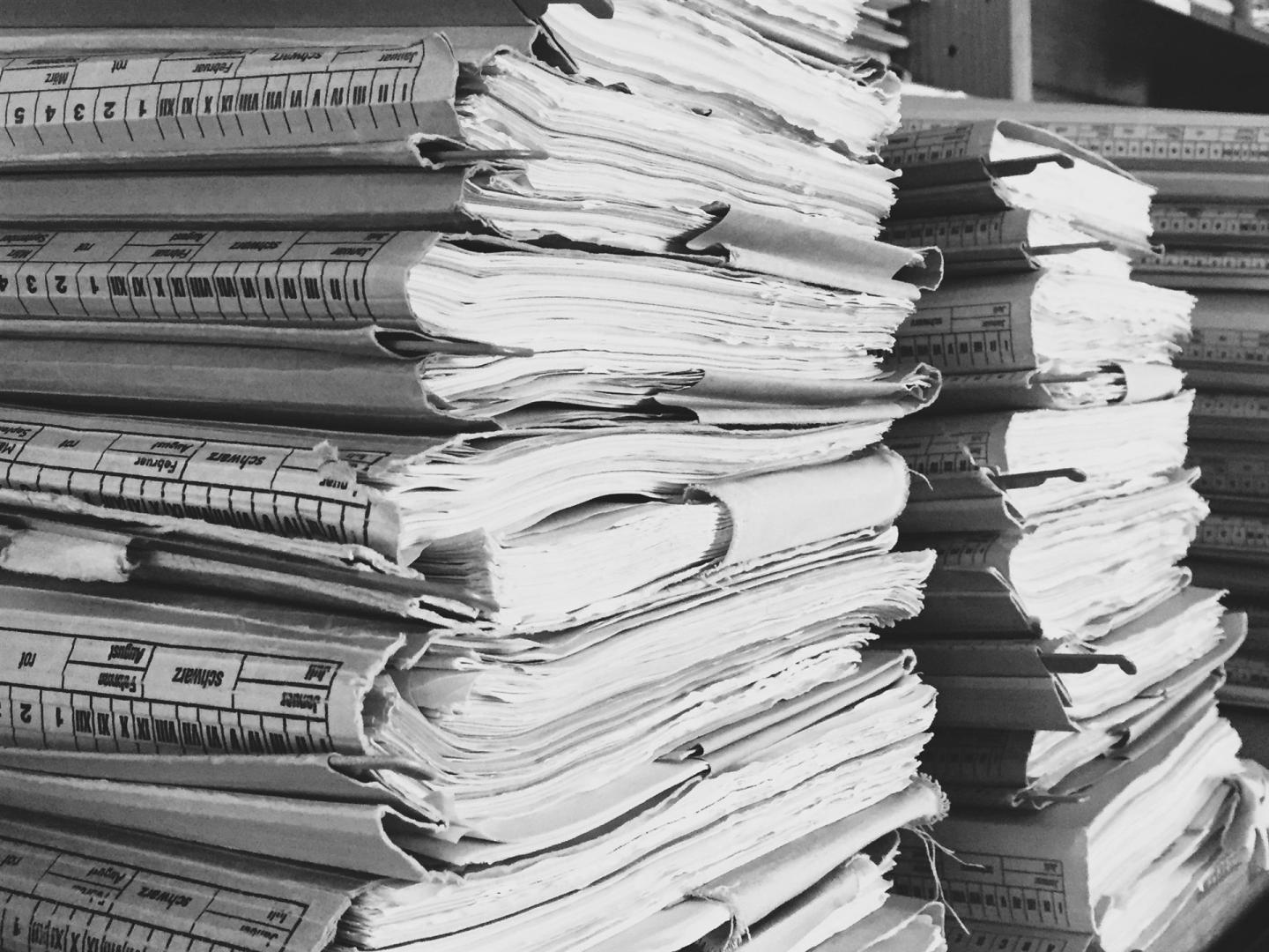 Ein großer Stapel alter, gestapelter Dokumente, Bücher und Zeitungsseiten, die einen Archiv- oder Bibliotheksbereich füllen.