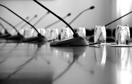 Eine Reihe von Mikrofonen und Kabeln auf einem langen, reflektierenden Konferenztisch.